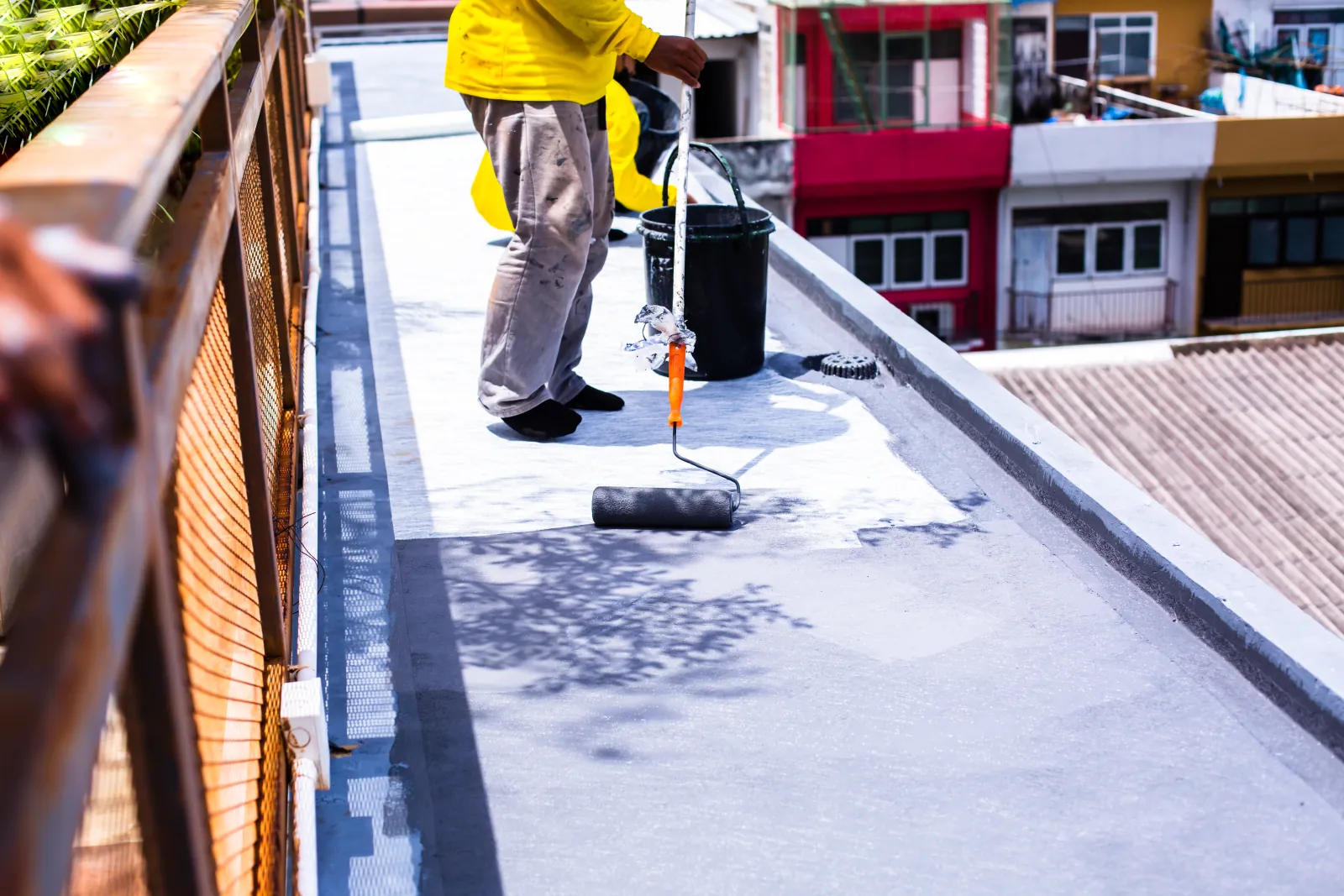 Roofer rolling a reflective restoration coating across a flat roof